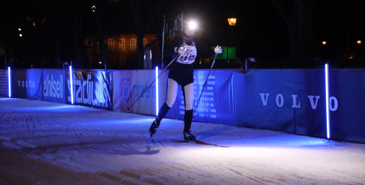 Cross-country skier skiing in a lit trail on a dark winter evening.