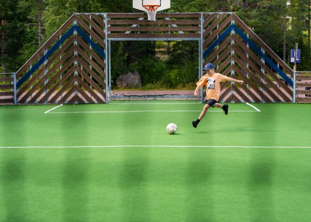 Child playing soccer on an artificial turf field with goal and basketball hoop.