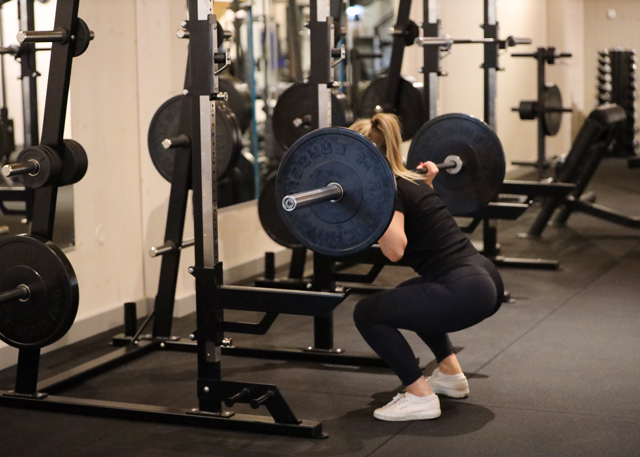 Person doing squats with a barbell in a gym.