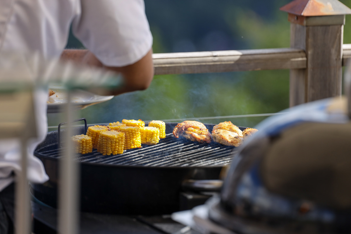Close-up of a barbecue where chicken and corn cobs are being grilled outdoors.
