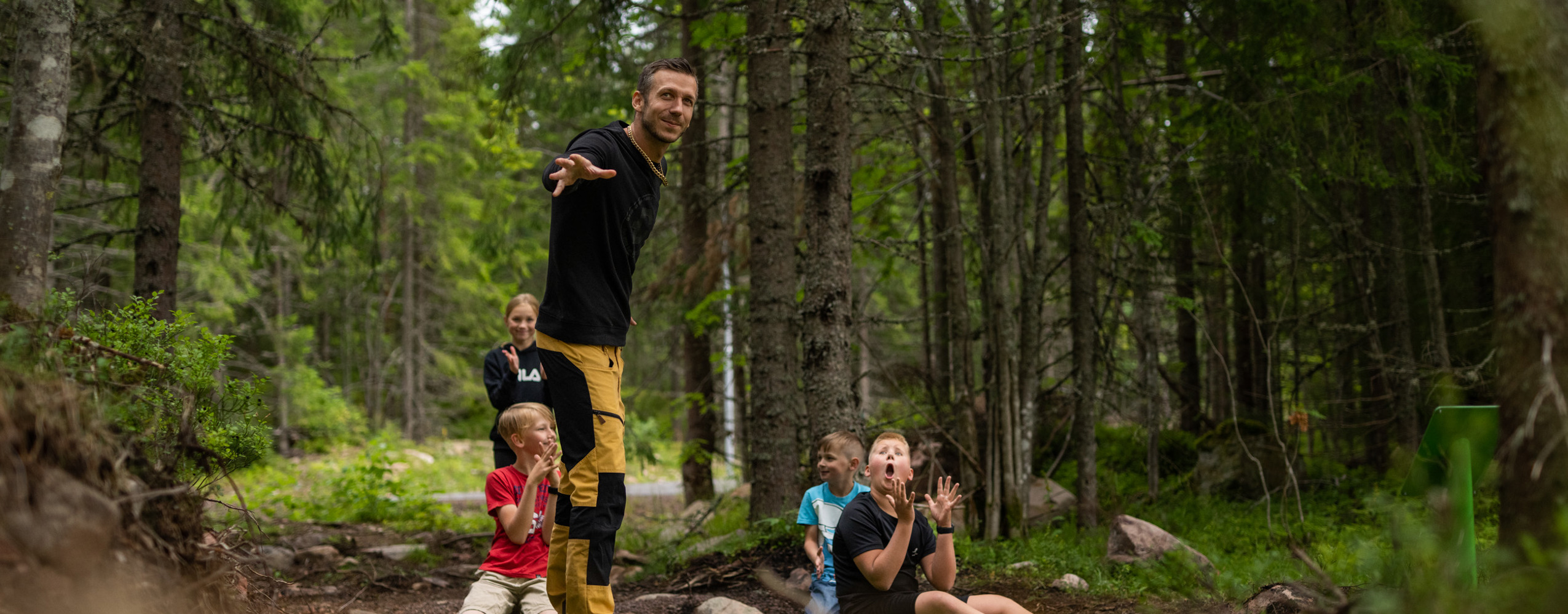 En familj spelar discgolf i Orsa Grönklitt - pappan kastar discen med glädje, medan barnen hejar på i den vackra naturen.