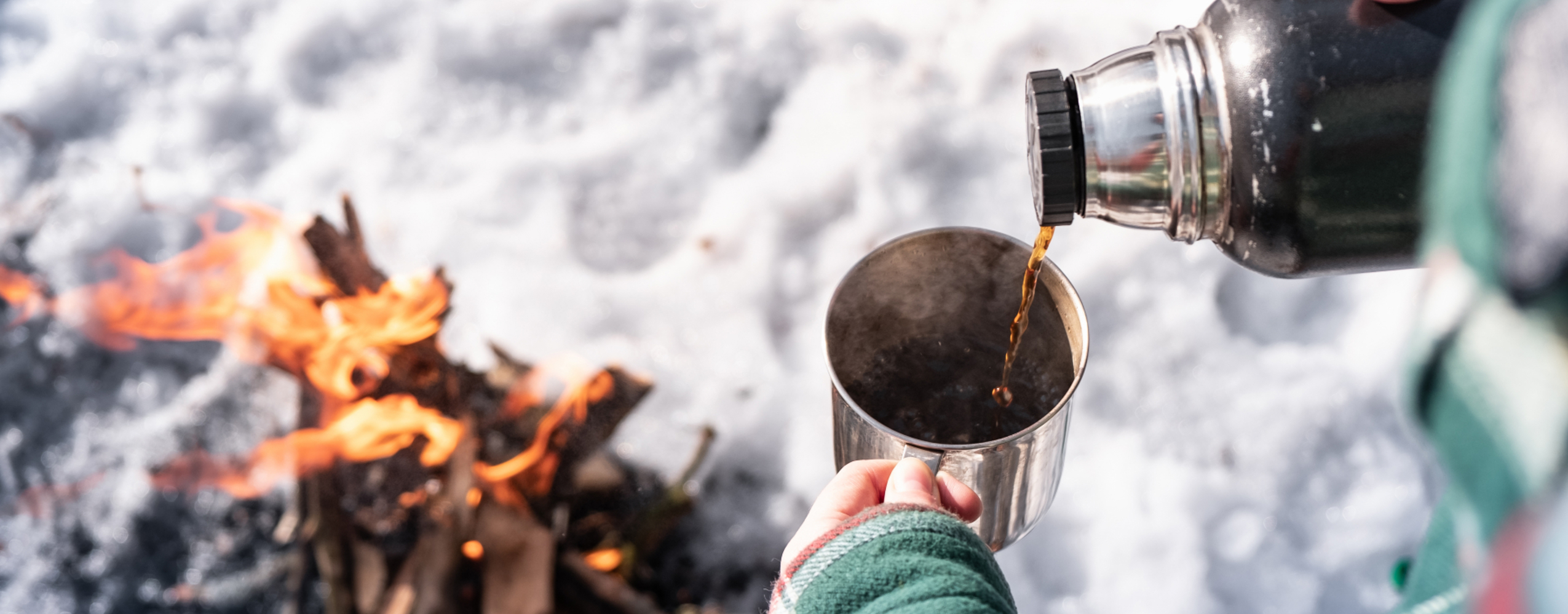 Kvinna som dricker kaffe ur termos över öppen eld i Orsa Grönklitt